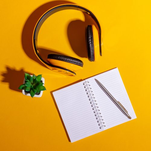 Desktop with yellow wireless headphones and an open notebook on a bright yellow background
