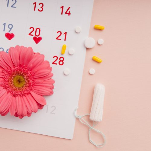 Menstruation calendar with marks, pills, hygiene tampons and flower. Top view. Woman's protection concept.